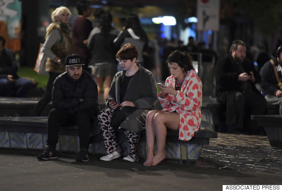 People evacuated from buildings along Dixon Street check their mobile phones while sitting on a bench in Wellington after a 6.6 earthquake based around Cheviot in the South island shock the capital, New Zealand, Monday, Nov. 14, 2016. A powerful earthquake struck New Zealand near the city of Christchurch early Monday, with strong jolts causing some damage to buildings over 200 kilometers (120 miles) away in the capital, Wellington. (Ross Setford/SNPA via AP)